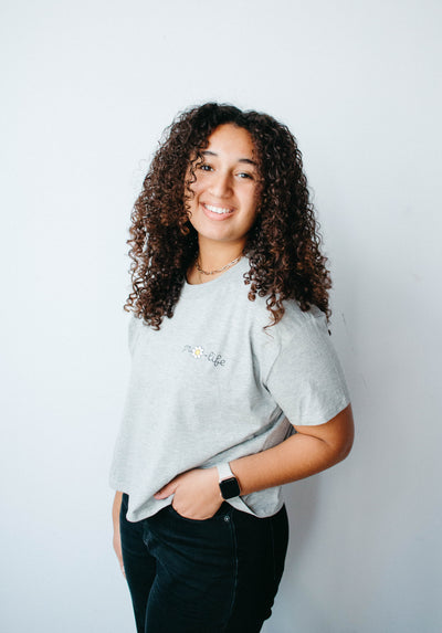 A heather gray crop tee with pro-life written near the top right shoulder with a daisy replacing the o in pro.